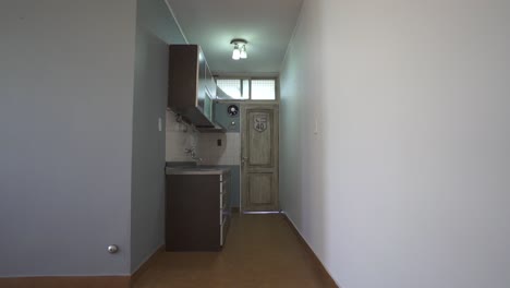 clean narrow kitchen hallway with overhead cabinets, sink, white walls, and a wooden door at the end, minimal modern design, no people, soft natural light, slow pan motion