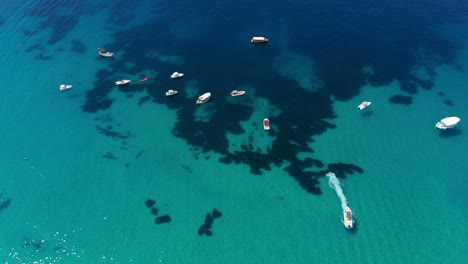 boats floating on calm turquoise waters in albania, with shadows from underwater reefs