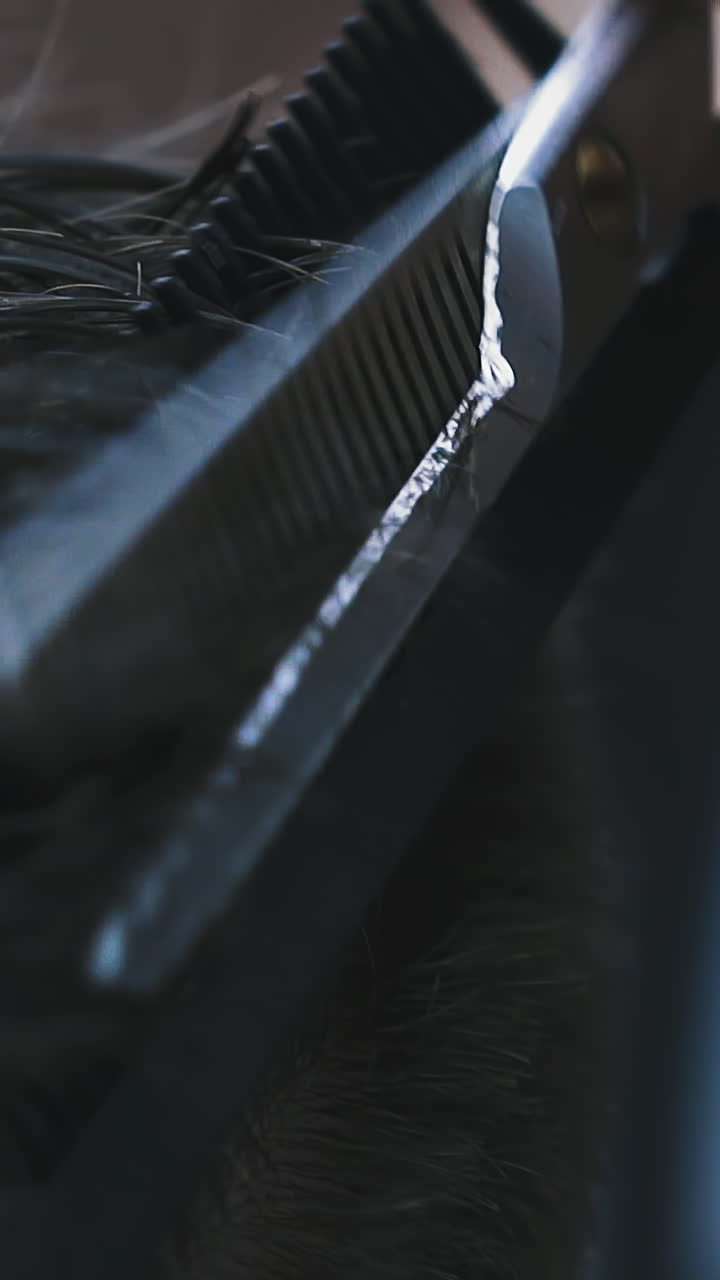 CU, slow motion: skilled hairdresser does haircut to male client with dark hair using comb and scissors in barbershop backside extreme close view