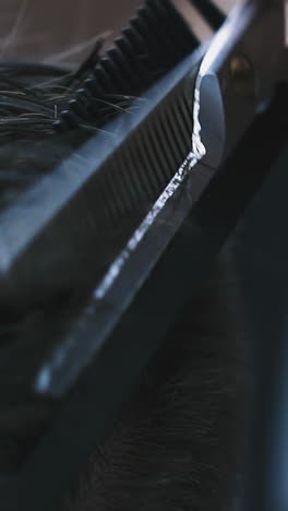 cu, slow motion: skilled hairdresser does haircut to male client with dark hair using comb and scissors in barbershop backside extreme close view