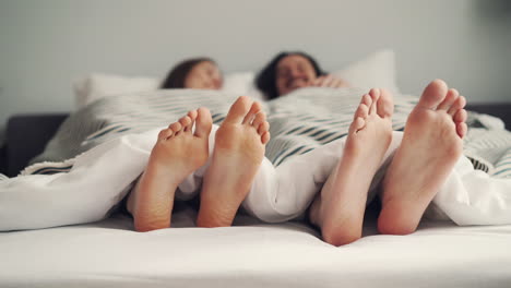 couple feet peeking out from under blanket in bed