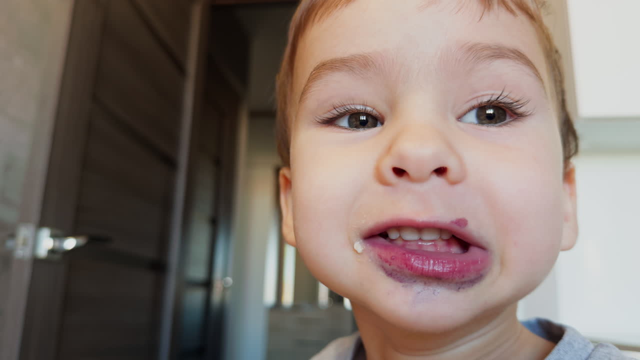Face of an adorable toddler boy with spots around mouth. Kid opens mouth talking. Close up.