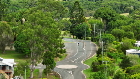 drone view of cyclist riding bike through scenic small rural town in australia, telephoto slow motion 4k