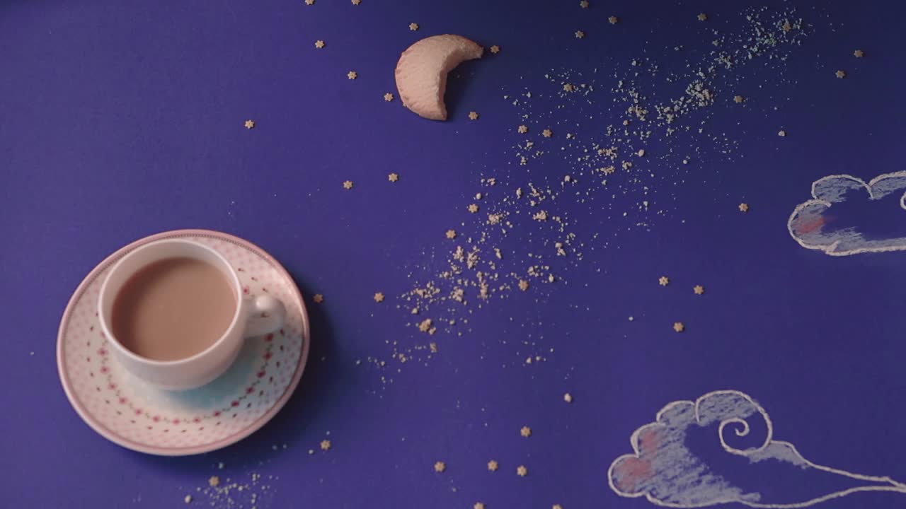 누군가가 밤하늘의 형태로 만들어진 테이블에서 커피 컵을 클로즈업으로 가져옵니다.