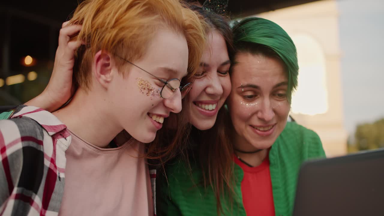 close-up de tres chicas felices con cabello largo corto en ropa brillante mirando algo en una pantalla de portátil durante su paseo en el verano