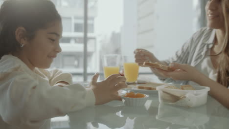 careful mother making toast with jam for little daughter on breakfast