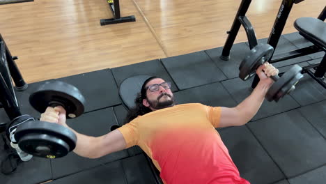 hombre latino con barba y cabello largo realizando ejercicio de crucifijo con pesas