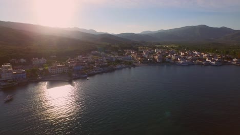 Aerial:-Small-fishing-town-with-Greek-flag-on-Samos-island,-Greece