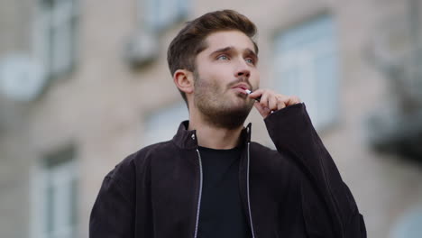 hombre guapo vaporizando al aire libre. hombre pensativo fumando cigarrillos electrónicos en la calle de la ciudad