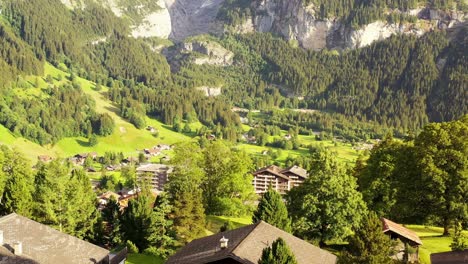 aerial forward ascending drone shot of countryside cottages and wooden cabin houses on green grassy meadow edge view to mountain peaks of grindelwald village in swiss alps at golden hour