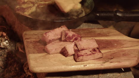 Fried-ham-slices-removed-from-iron-pan-onto-cutting-board-by-campfire