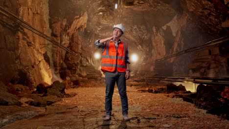 full body of asian male engineer with safety helmet showing thumbs down gesture and shaking his head while standing in underground mine tunnel