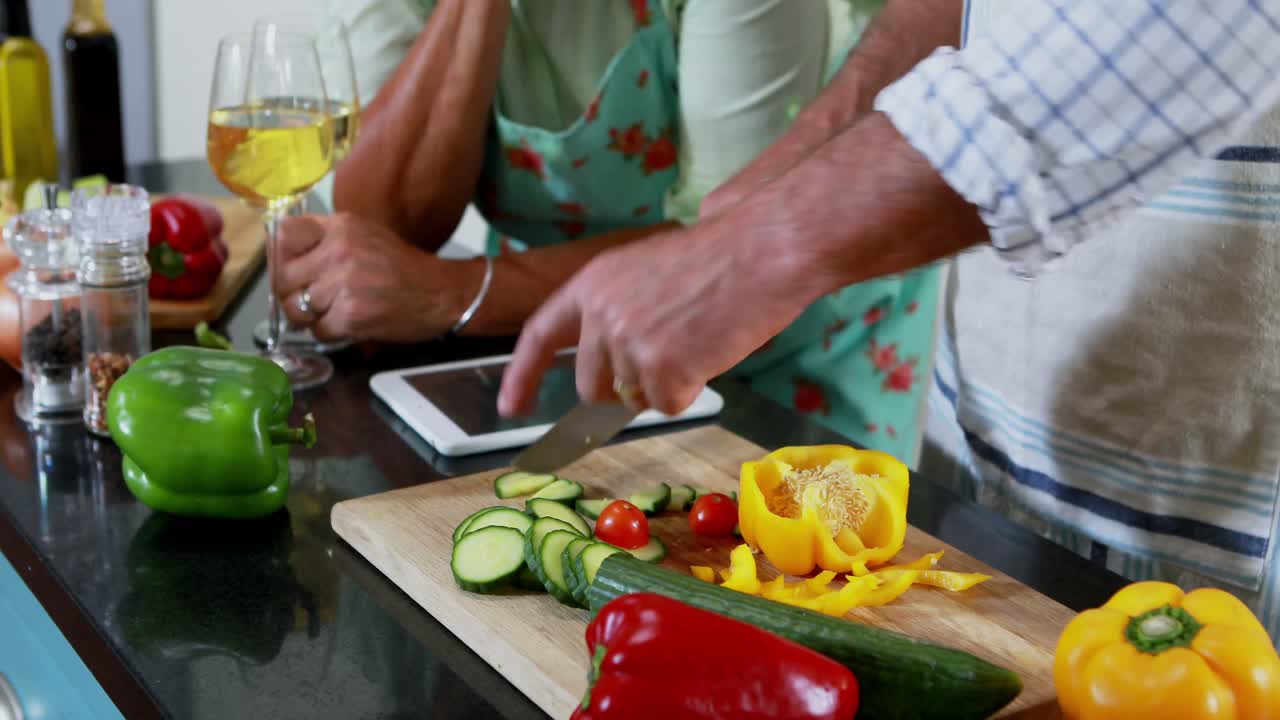 sección media de una pareja mayor cortando verduras en la cocina 4k