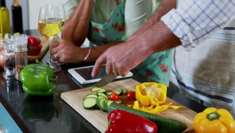 Mid-section-of-senior-couple-cutting-vegetables-in-kitchen-4k