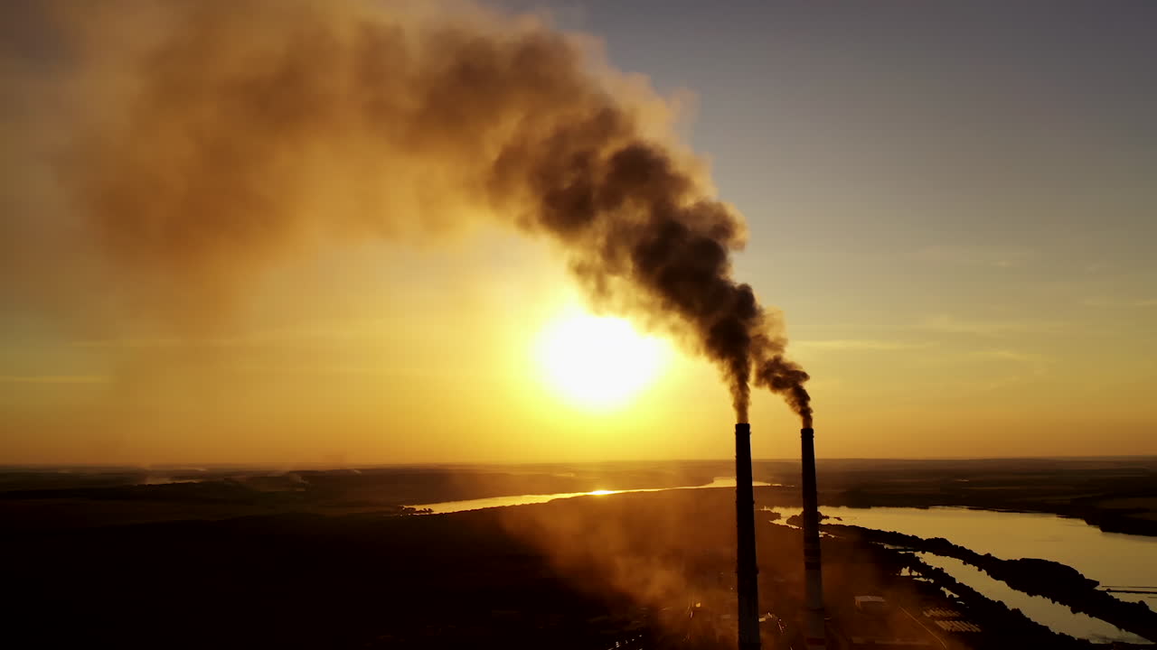 Dirty emissions in nature at sunset. Thick smoke coming from industrial pipes on the yellow sun setting background. Ecological disaster.