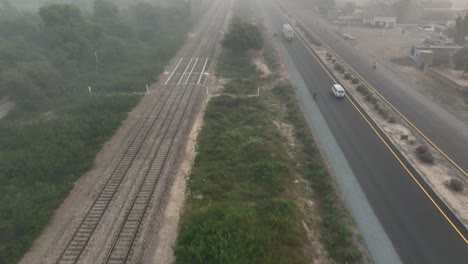 Vista-Aérea-De-Sahiwal-A-Multan-Road-Con-Un-Vehículo-Pasando-Durante-Una-Noche-De-Niebla-En-Punjab,-Pakistán