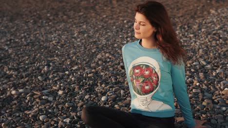 woman meditating on a pebble beach at sunset
