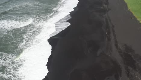 black sand beach with waves in vik, iceland with drone video above moving back