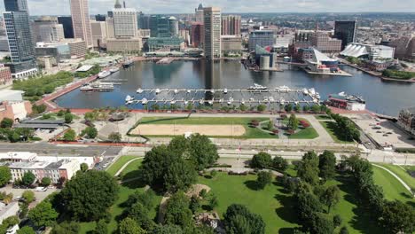 aerial tilt up reveals federal hill and downtown baltimore financial district and inner harbor, american flag, sand volleyball court, boats ships and yachts in harbour, aquarium, tourist attractions