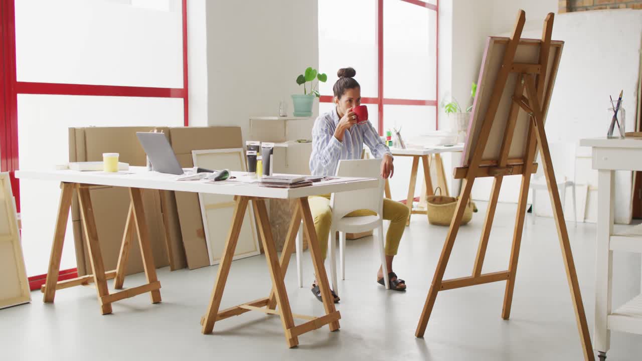 video de una feliz diseñadora biracial bebiendo café en el estudio