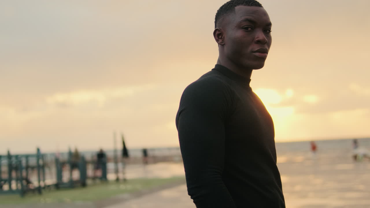 Jovem homem negro em pé à beira-mar ao pôr do sol