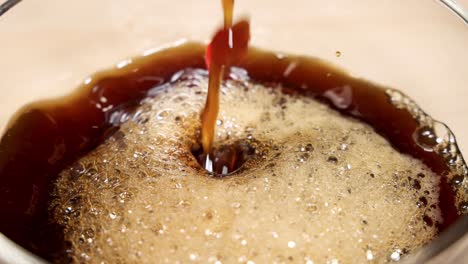 close-up of coffee being poured into a glass, creating rich foam and bubbles, set against a black background
