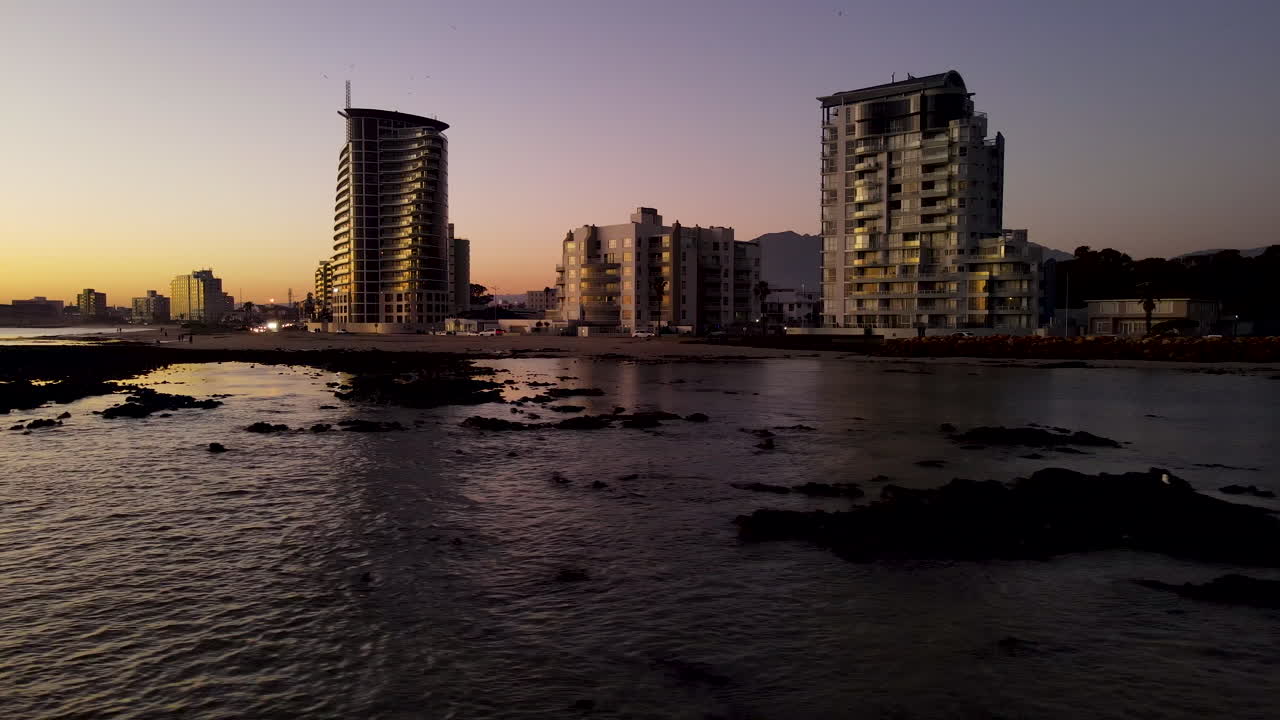 puesta de sol aérea sobre arrecifes poco profundos frente a la costa con apartamentos frente al mar