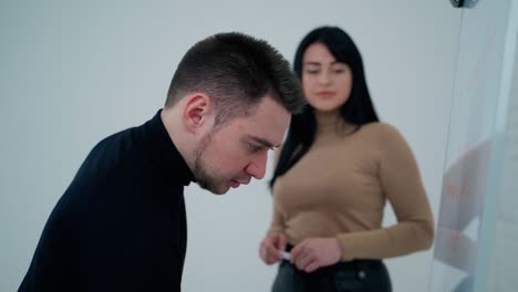 man and woman near the board indoors. young man writing on a white board with a marker. business workers think about new project.