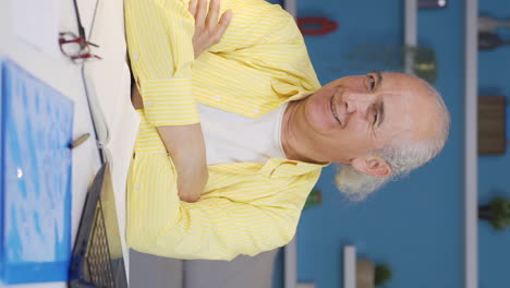 Vertical-video-of-Home-office-worker-old-man-looking-smugly-at-camera.