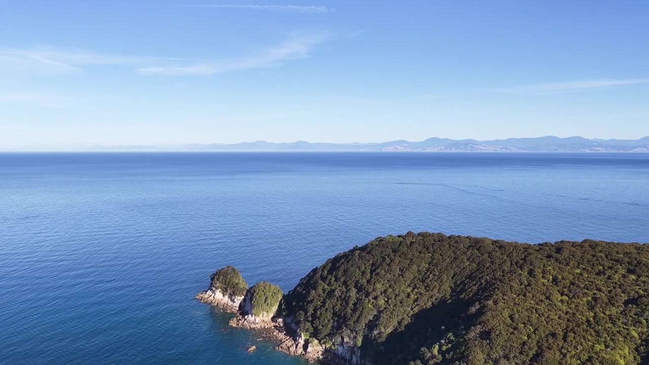 Veduta aerea di un promontorio costiero frastagliato sull'Isola del Sud della Nuova Zelanda, circondato da calme acque blu dell'oceano che si estendono verso l'orizzonte lontano.