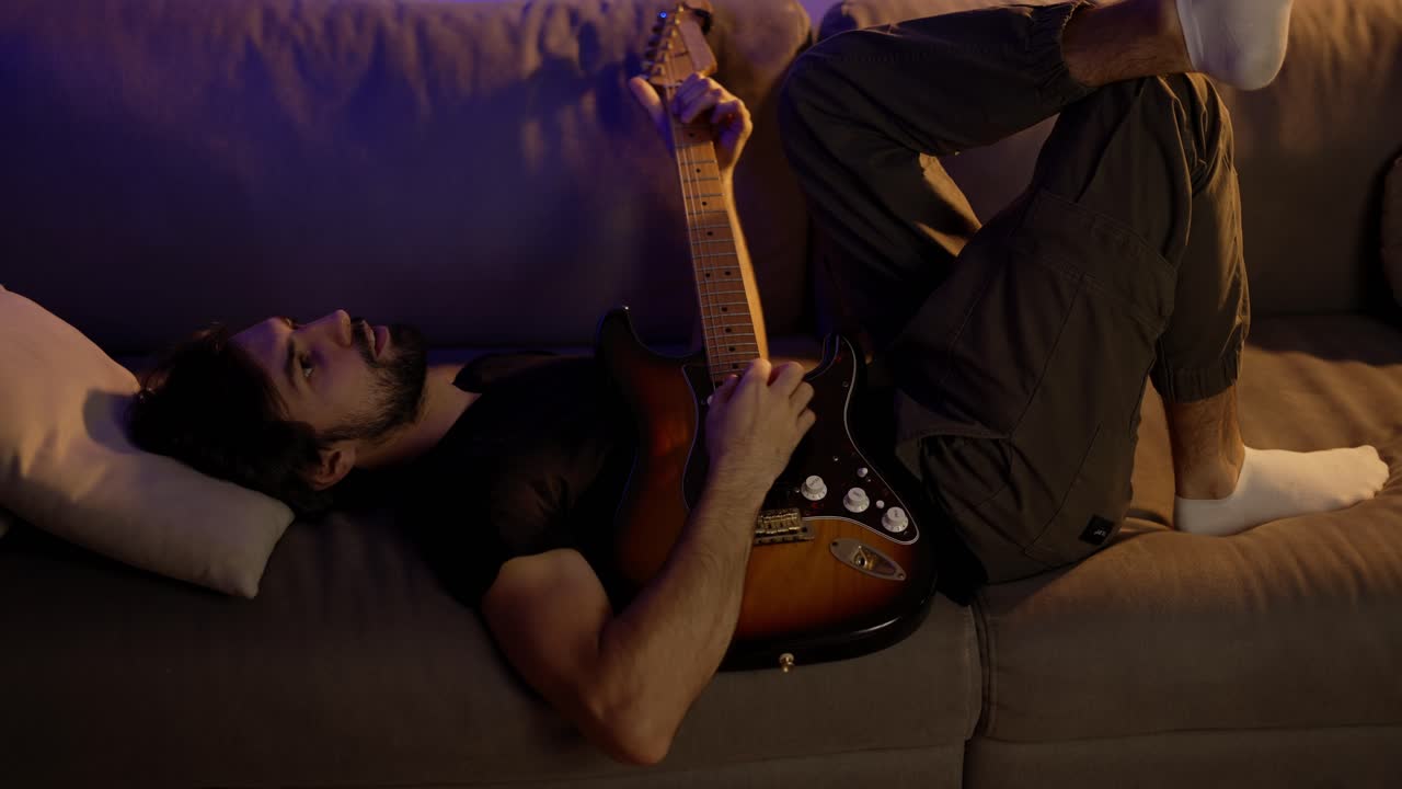 hombre componiendo música en la guitarra mientras está acostado en el sofá