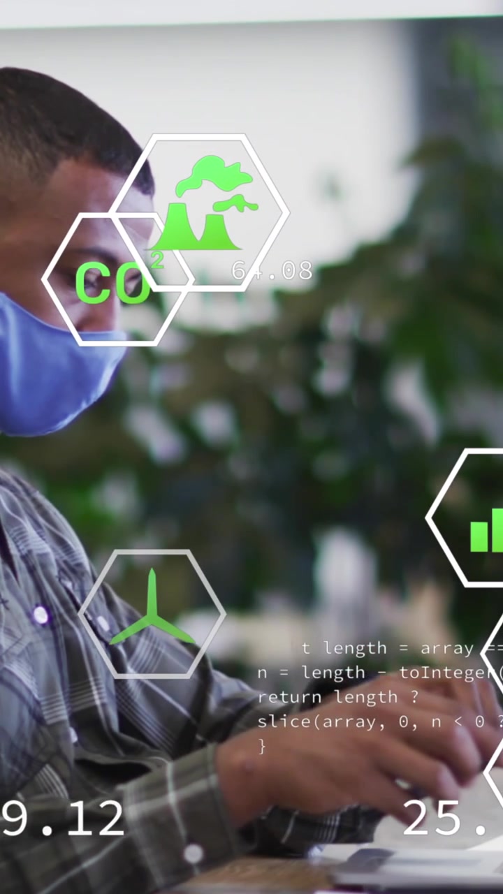 Animation of ecology icons over african american businessman wearing face mask and using computer