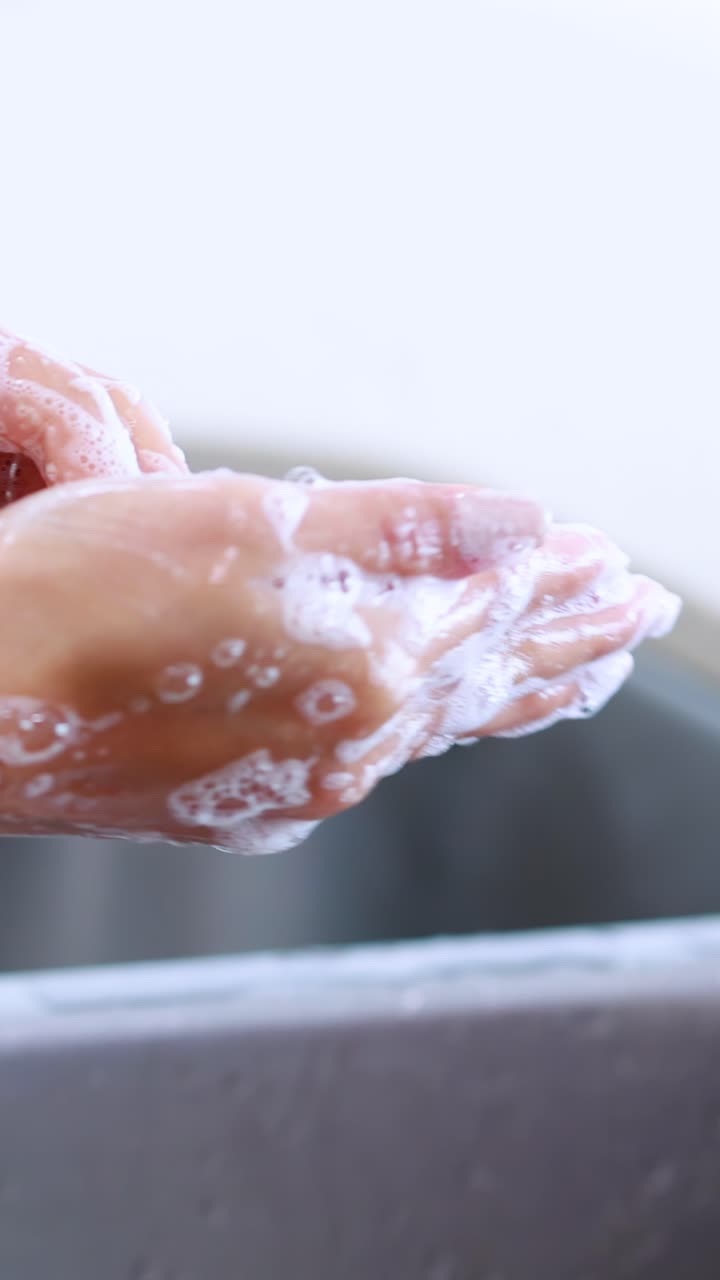 Sequenza ravvicinata di mani che si insaponano e si sciacquano sotto l'acqua corrente in un ambiente cucina luminoso e moderno con illuminazione naturale.