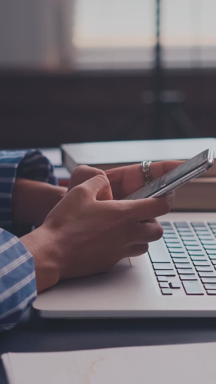 Close up of hands using a smartphone over a laptop keyboard in a modern office
