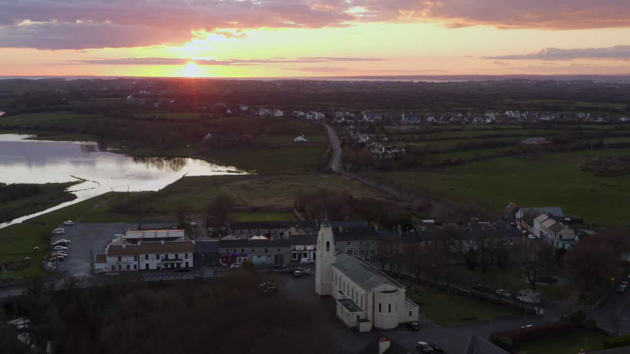 Clarinbridge rooftops and landscape lit by soft sunset light during golden hour aerial, pullback from church steeple
