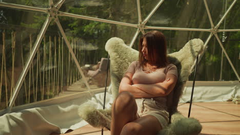 dama deprimida con los brazos cruzados descansa en un sillón de piel de oveja en una habitación con ventanas panorámicas en un hotel de país turístico. alquiler de vivienda temporal para recreación en la naturaleza