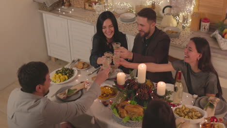 group of happy friends sitting at table and making a toast before eating christmas meal at home 1