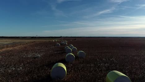 Sweeping-Drone-Aerial-shot-of-a-Midwestern-cotton-farm-with-fresh-bales-of-harvested-cotton-wrapped-in-bright-yellow-material-against-a-blue-open-sky