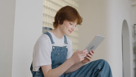 Side-View-Of-Girl-Sitting-On-The-Stairs-Using-A-Tablet-At-Home