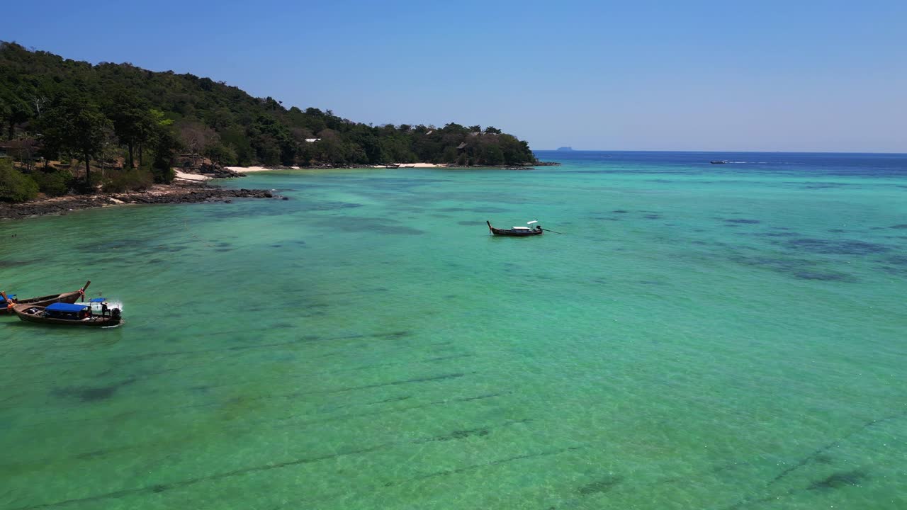 Aerial view of a tropical island beach with turquoise water showing long tail boats waiting for tourists in thailand