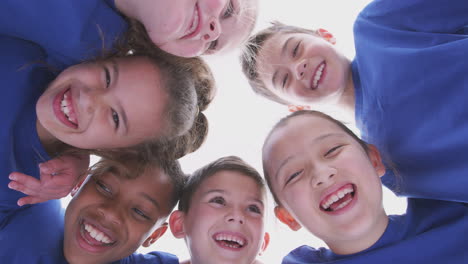 Low-Angle-View-Looking-Up-Into-Faces-Of-Children-In-Huddle-On-Sports-Day