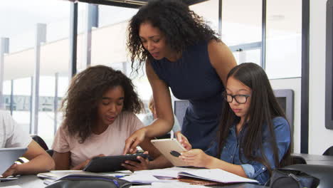 teacher helping teenage schoolgirls with technology in class