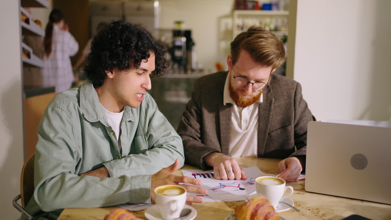 dos hombres discutiendo negocios sobre café y gráficos en un café