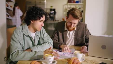 two men discussing business over coffee and charts in a cafe