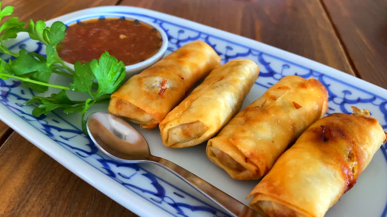 Lumpia tradisional dengan saus cabai manis di atas piring putih dan biru di restoran Thailand, bidikan bergerak ke atas 4K.