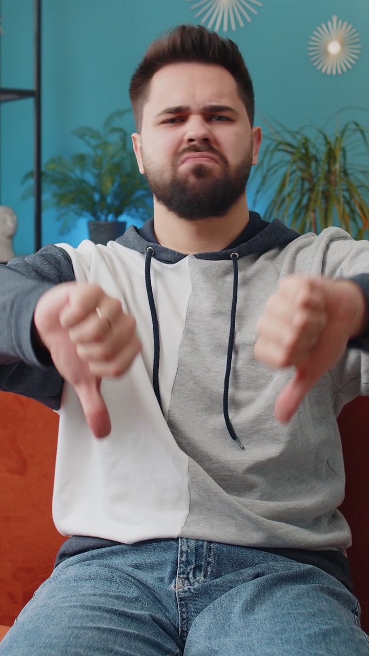 Upset caucasian man showing thumbs down dislike bad work disapproval dissatisfied feedback at home