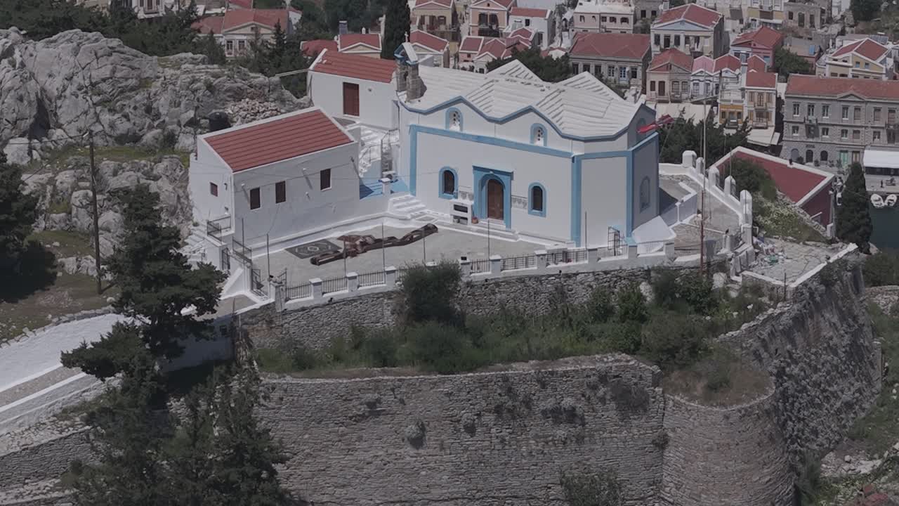 Cinematic telephoto drone reveal with foreground movement and compressed background of Symi’s colorful architecture