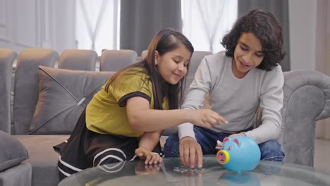 Happy-Indian-siblings-saving-money-and-putting-coins-in-piggy-bank