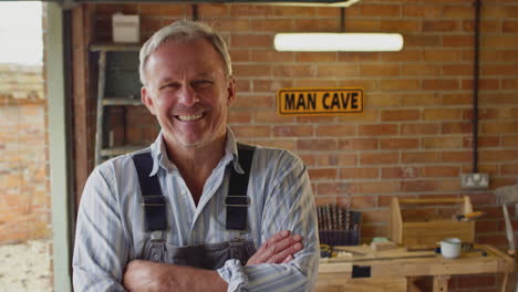 portrait of smiling mature male wearing overalls in garage workshop