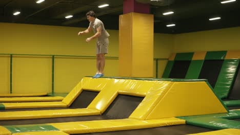 Yellow-covered-trampoline-for-young-sportive-people.-Athletic-male-performs-front-somersaults-hopping-off-the-platform.-Youth,-sport,-gymnastics.